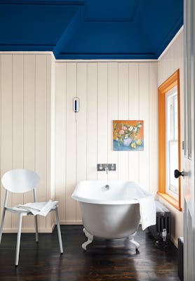 Bathroom with paneled off-white (Flint) walls and a contrasting deep blue ceiling with a bathtub and chair by the window.