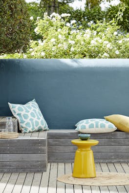 Outside seating area with an Air Force Blue back wall and a wooden panelled bench with cushions.