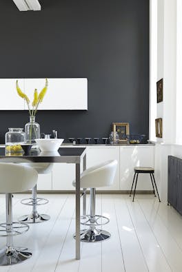 Rich black (Lamp Black) kitchen with bright white units and stools next to a black table.