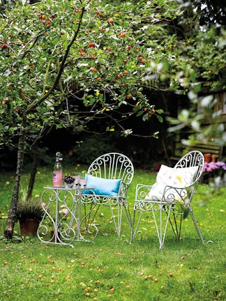 Two metal garden chairs painted in the grey-green shade 'Normandy Green', sitting on grass next to a small tree.