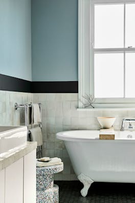 Bathroom with pale blue (Bone China Blue) upper walls and white tiles underneath, next to bathtub, window and sink.