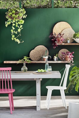 Outside dining room table and chairs with a dark green wall (Puck) with wooden shelves.