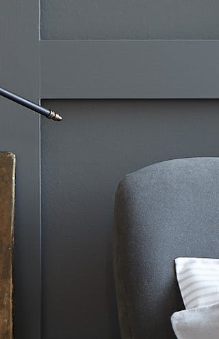 Close-up of a dark grey paneled wall painted in 'Scree', behind a bed with a grey headboard.