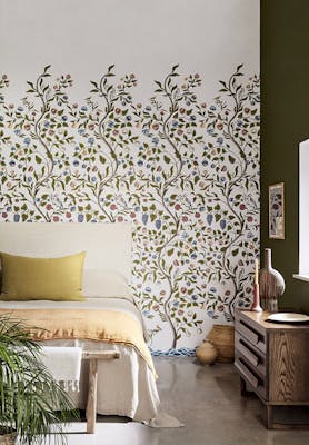 Bedroom with off white floral mural wallpaper (Mandalay - Ceviche) with a bed, sideboard and plant. 