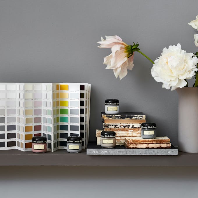 The Little Greene color card in front of a grey wall displayed alongside books, flowers and Little Greene sample pots.