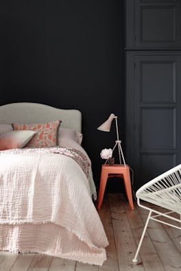 Bedroom painted in blue black 'Basalt' with a light pink bed and a contrasting bright orange stool.