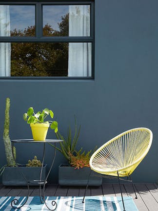 Outside dining area with a dark blue wall (Hicks' Blue) and bright yellow chair with a small table and plants.