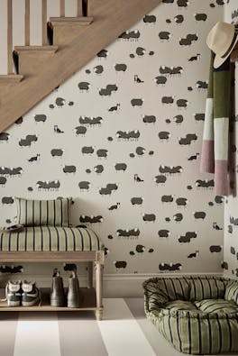 Hallway space featuring neutral dog and sheep print wallpaper (Nip & Lassie - Slaked Lime - Dark) with a dog sat in a bed on the right and stairs to the left.