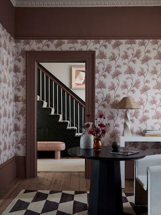 Living space featuring pink floral wallpaper (Mosaic Trail - Blush) with a dark table and chair with a door leading out to a staircase.