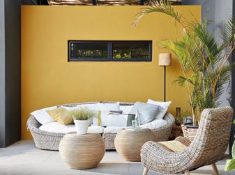 Outdoor lounge with a bright yellow (Yellow-Pink) wall behind a weave sofa, alongside a dark grey (Scree) wall to the right. 