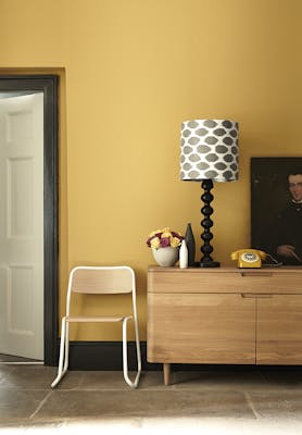 Hallway painted in mustard yellow (Yellow-Pink) with a wooden side table and chair.