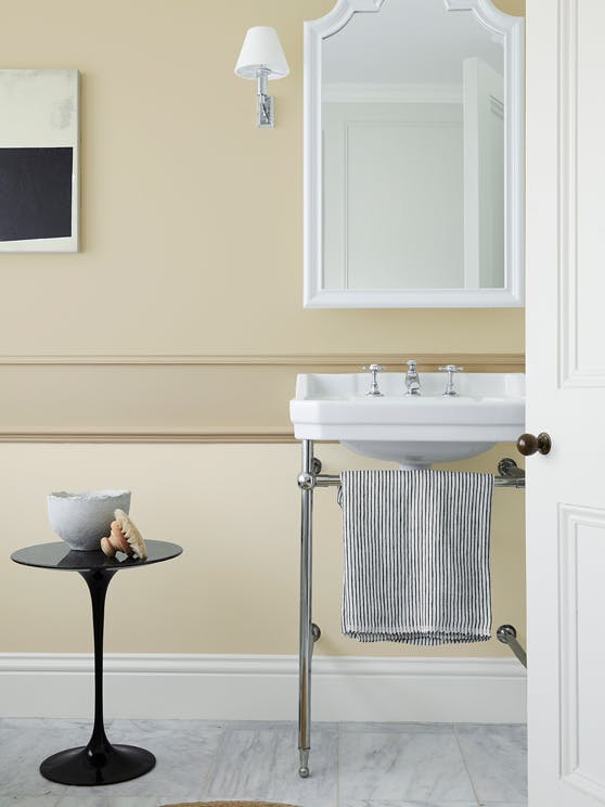 Bathroom painted in different shades of warm neutral 'Travertine' with a free standing sink, white mirror and small table.