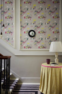 Bottom of stairs with grey bird print wallpaper (Voliéres - French Grey) and a small table with yellow gingham tablecloth.