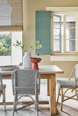 Golden yellow (Bath Stone) dining space with contrasting green shutters, a wooden dining room table and patterned chairs.