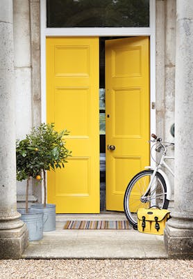 Front door painted in bright yellow 'Mister David' with two trees and a bike under pillars.