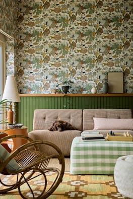 Living space featuring green wildlife print wallpaper (Animal Kingdom - Pea) with green paneling behind a sofa, foot stool and a rocking chair.