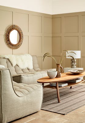 Paneled living space painted in warm neutral 'Travertine' with two sofas and a wooden coffee table.