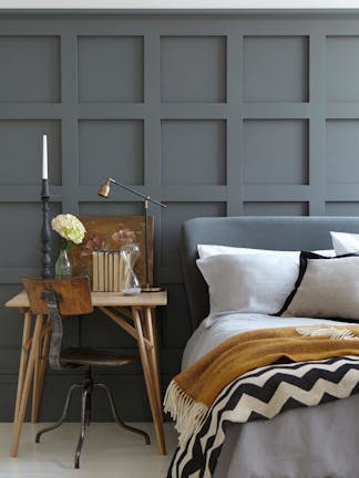 Paneled bedroom painted in dark grey 'Scree' with a small wooden desk next to a grey bed on a white floor.