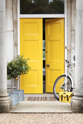 Front door painted in bright yellow 'Mister David' with two trees and a bike under pillars.