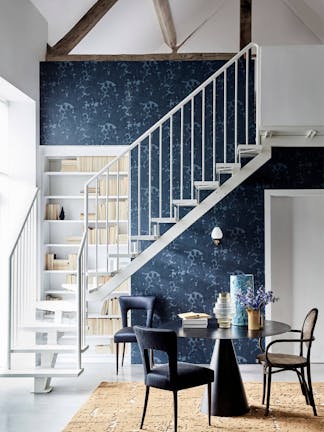 Hallway feauturing wallpaper with a scrolling foliage pattern (Tulip – Blue Black), and light grey stairs and balustrades.