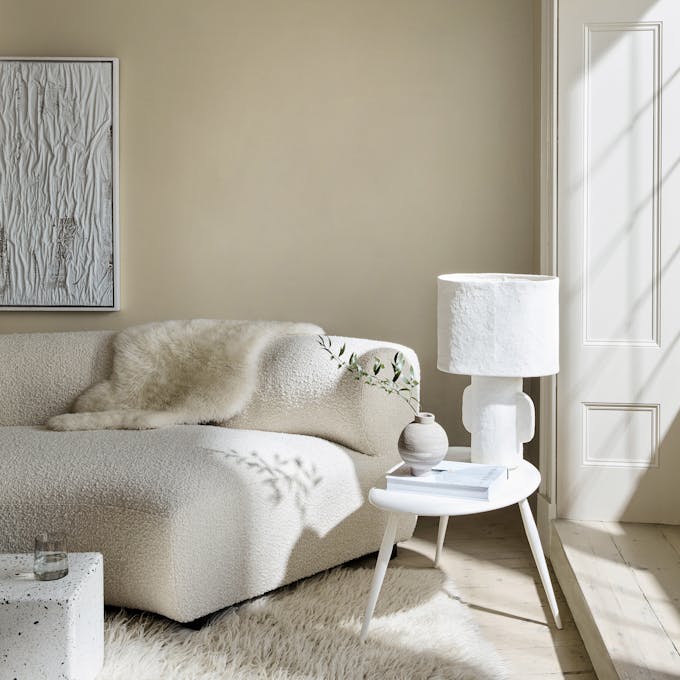 Living room in 3 different neutral shades (Silent White) with a sofa, table and lamp next to a window.