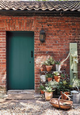 Brick exterior with a dark green (Goblin) door with several potted plants and a pebbled floor.