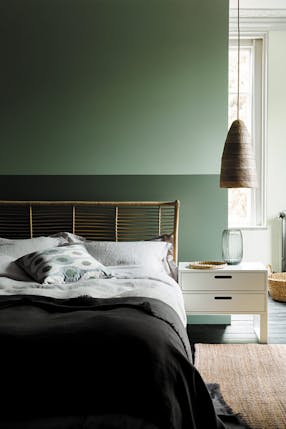 Bedroom with a wall painted half and half in two shades of green, behind a bed and white side table.