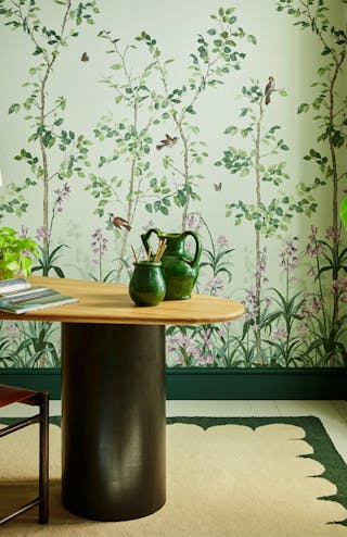 National Trust green floral mural wallpaper featuring birds and butterflies (Bird & Bluebell - Pea Green) behind a wood desk.