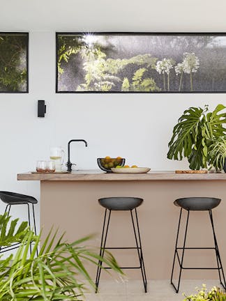 Outside breakfast bar with the back wall painted in off white shade 'Linen Wash' and the island painted in soft pink shade 'Masquerade' with two black stools and plants surrounding.