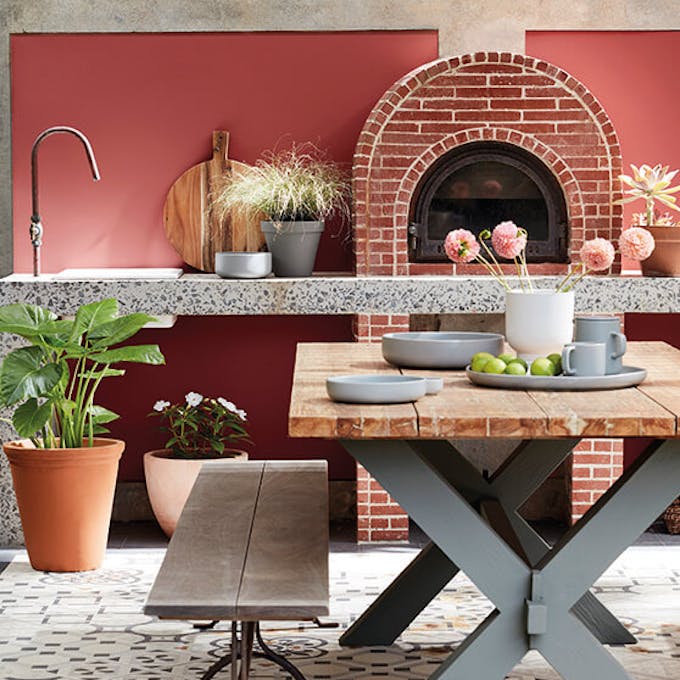 Outdoor kitchen painted in deep terracotta red 'Tuscan Red' with brickwork, plants and a basket.