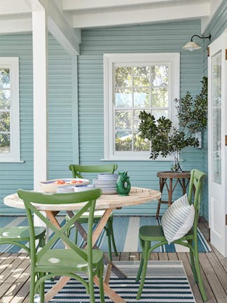 Outside dining area with cladded wall painted in pale blue (Celestial Blue) and a dining room table with green chairs.