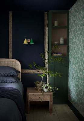 Bedroom with a dark blue back wall (Dock Blue) and the right wall in a pale green leafy wallpaper (Beech Nut - Rubine).