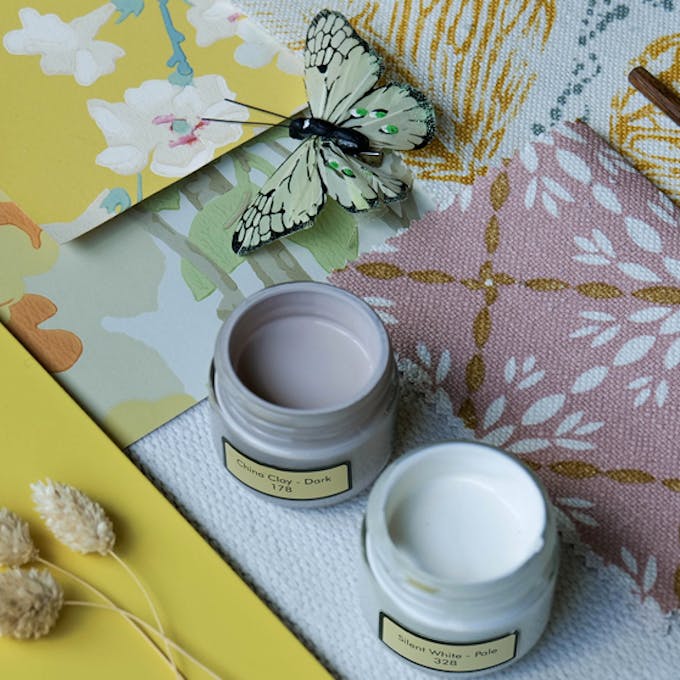 Two Little Greene paint sample pots open and placed on a moodboard with natural elements and wallpaper samples.