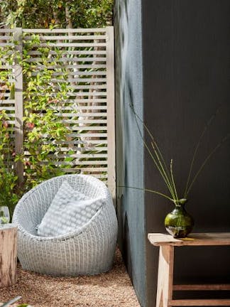 Garden with a bean bag chair placed next to a dark off-black wall painted in 'Obsidian Green' and in front of a wooden fence.