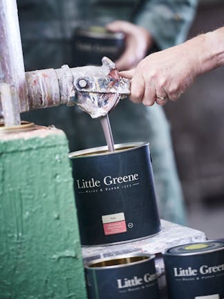 A hand pulling a lever on a factory machine to fill up a black Little Greene paint tin with Pink Aluminium Wood Primer.