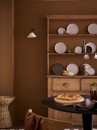 Dining space painted in orange-brown shade 'Galette' with a wooden dining table and a large wooden dresser and plates.