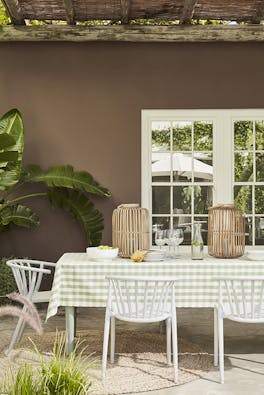 Outside dining table and chairs with the back wall painted in rich chocolate shade 'Scullery' with white panelled doors and a large plant.