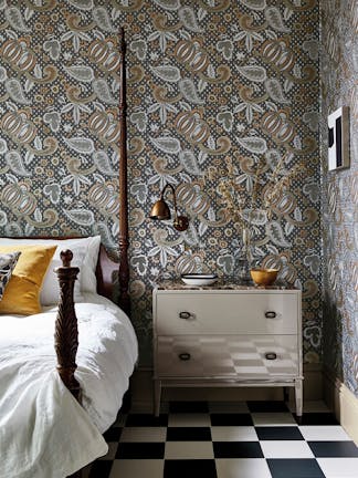 Bedroom with a paisley wallpaper (Pomegranate - Prophet) and a four poster bed with drawers and a black chair.