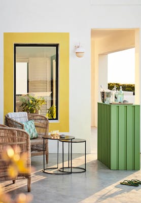 Outside bar in bright green (Garden) with wicker chairs, a drinks table and white walls with Indian Yellow highlights.