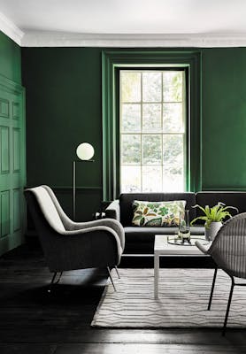 Living space painted in dark green (Puck) with a grey sofa, armchair and a white table on a rug.