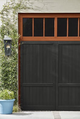 Panelled exterior doors painted in deep black 'Jack Black' with burnt orange (Heat) windows above and greenery on the walls.