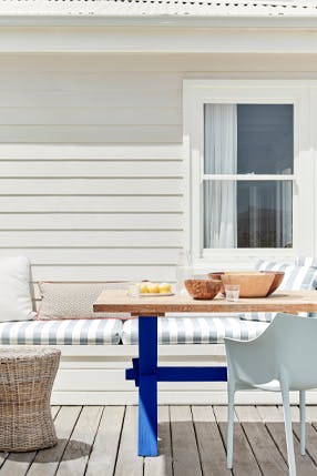 Outdoor dining area with horizontal wood panelled walls painted in Linen Wash white, with bench seating and a blue dining table