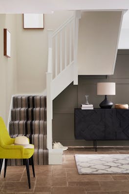 Home entryway with panelling in warm brown shade 'Attic II' and carpeted stairs with pale neutral walls and woodwork.