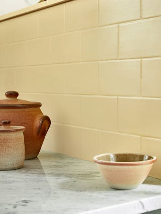 Close-up of light yellow kitchen tiles behind a marble kitchen top and three rustic-style bowls.