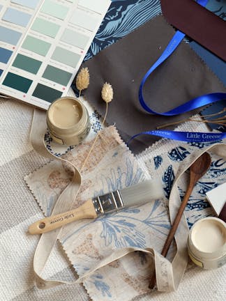 Little Greene Color Card open showing blue-green color swatches, alongside fabric samples, a paint sample pot and paintbrush.