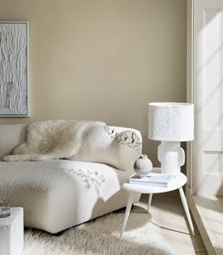 Living room in 3 different neutral shades (Silent White) with a sofa, table and lamp next to a window.