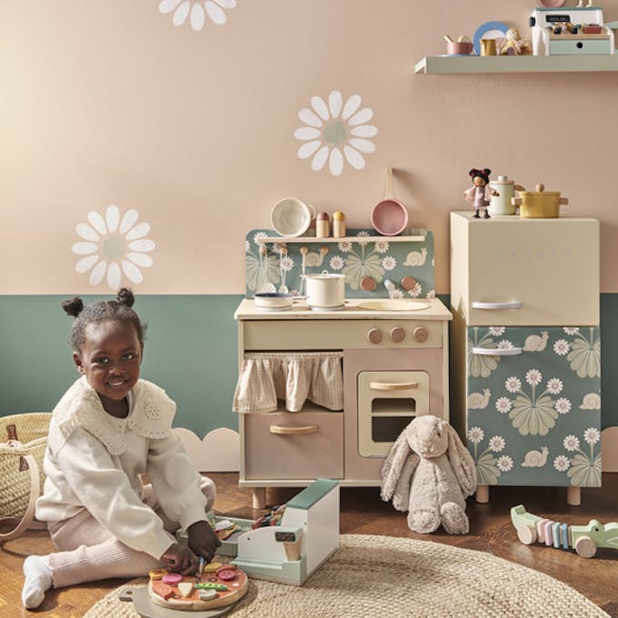 Playroom with pale pink (Masquerade) walls with a child playing with a toy cooker.