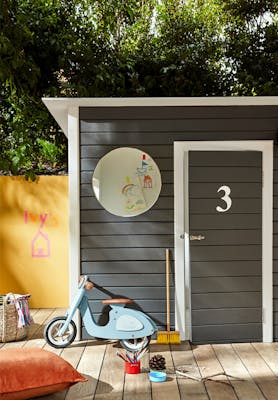 Dark grey (Scree) shed with toys outside and a bright yellow (Yellow-Pink) wall to the left.