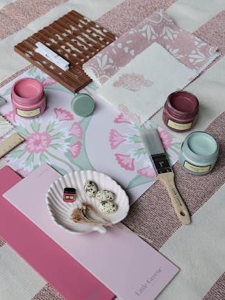 Pink and light green themed mood board featuring a floral patterned wallpaper sample, various fabric samples and color cards.