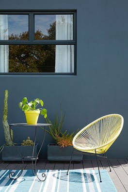 Outside dining area with a dark blue wall (Hicks' Blue) and bright yellow chair with a small table and plants.